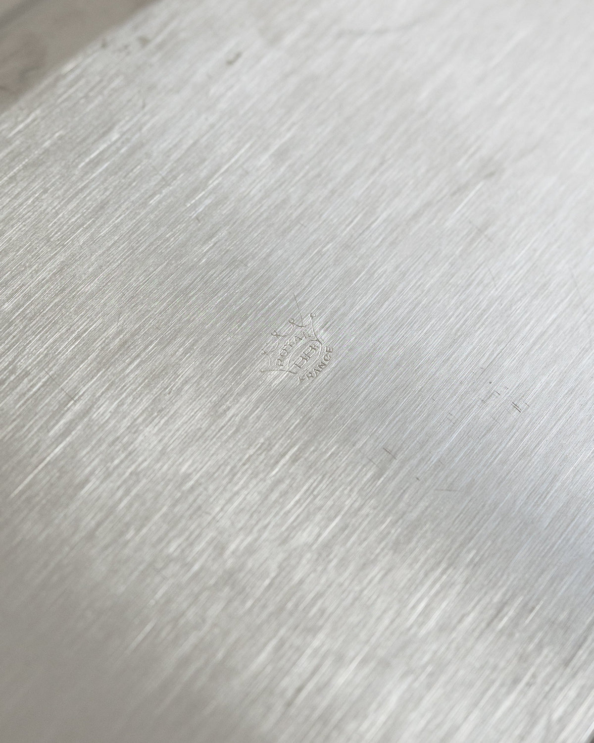 Close-up of a brushed silver metal surface with a faint embossed logo in the center.