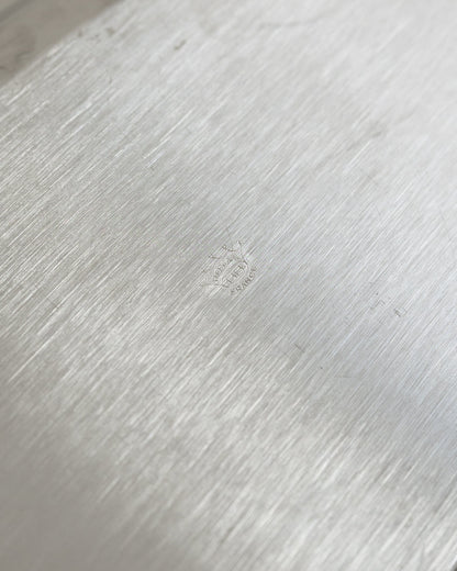 Close-up of a brushed silver metal surface with a faint embossed logo in the center.