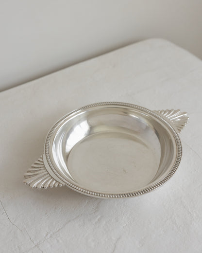 A small oval silver tray with decorative leaf-like side handles and a beaded rim, photographed on a light fabric surface against a plain off-white background.