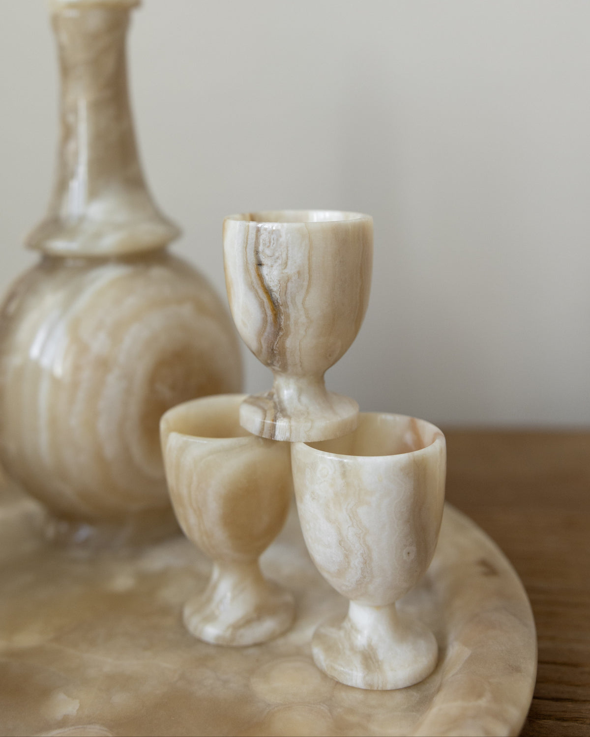 A set of polished onyx stone drinking vessels, including a decanter and two goblets, arranged on a matching stone tray against a soft neutral background.