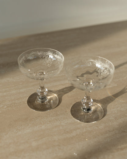 Two clear glass coupe cups with textured interiors, resting on a beige stone surface under warm natural sunlight.