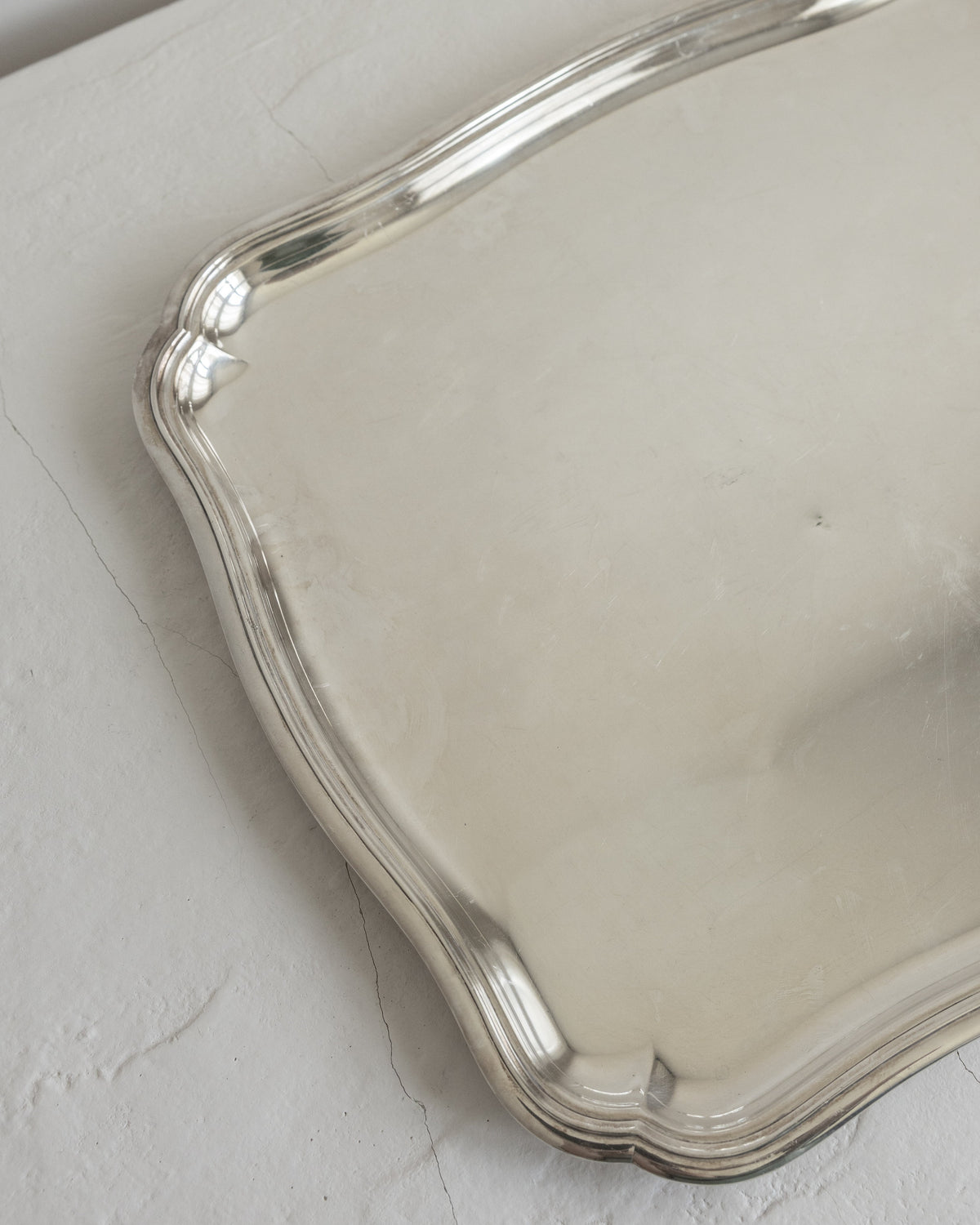 A close-up of a polished silver tray with a scalloped edge, resting on a textured off-white surface.