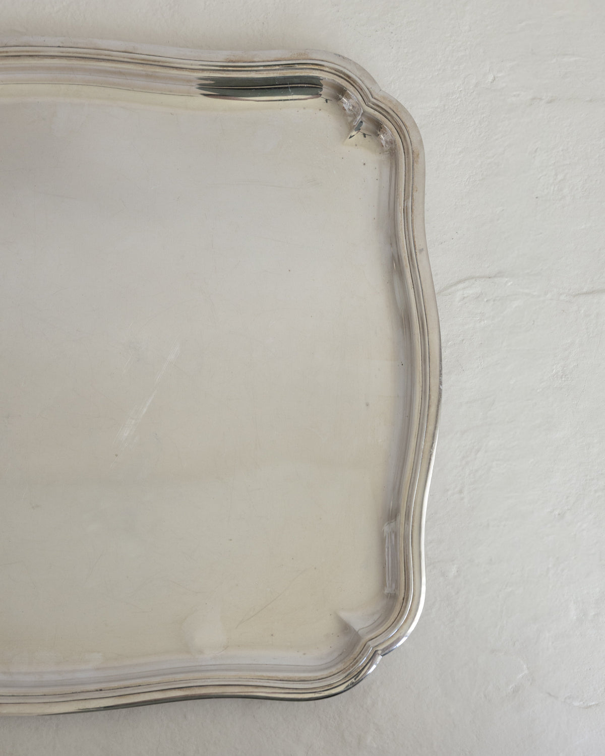 A close-up of a silver-toned metal tray with a scalloped edge, resting on a textured off-white surface.