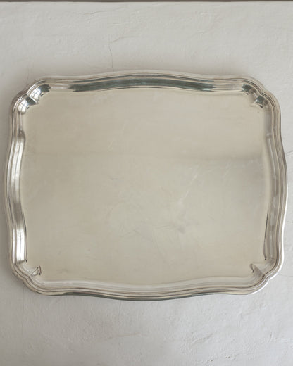 A rectangular silver serving tray with scalloped edges, photographed from above against a light gray textured background.