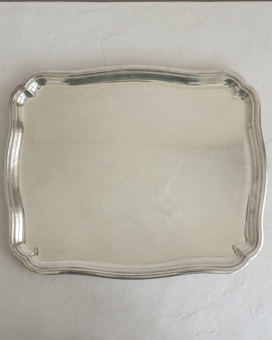 A rectangular silver serving tray with scalloped edges, photographed from above against a light gray textured background.