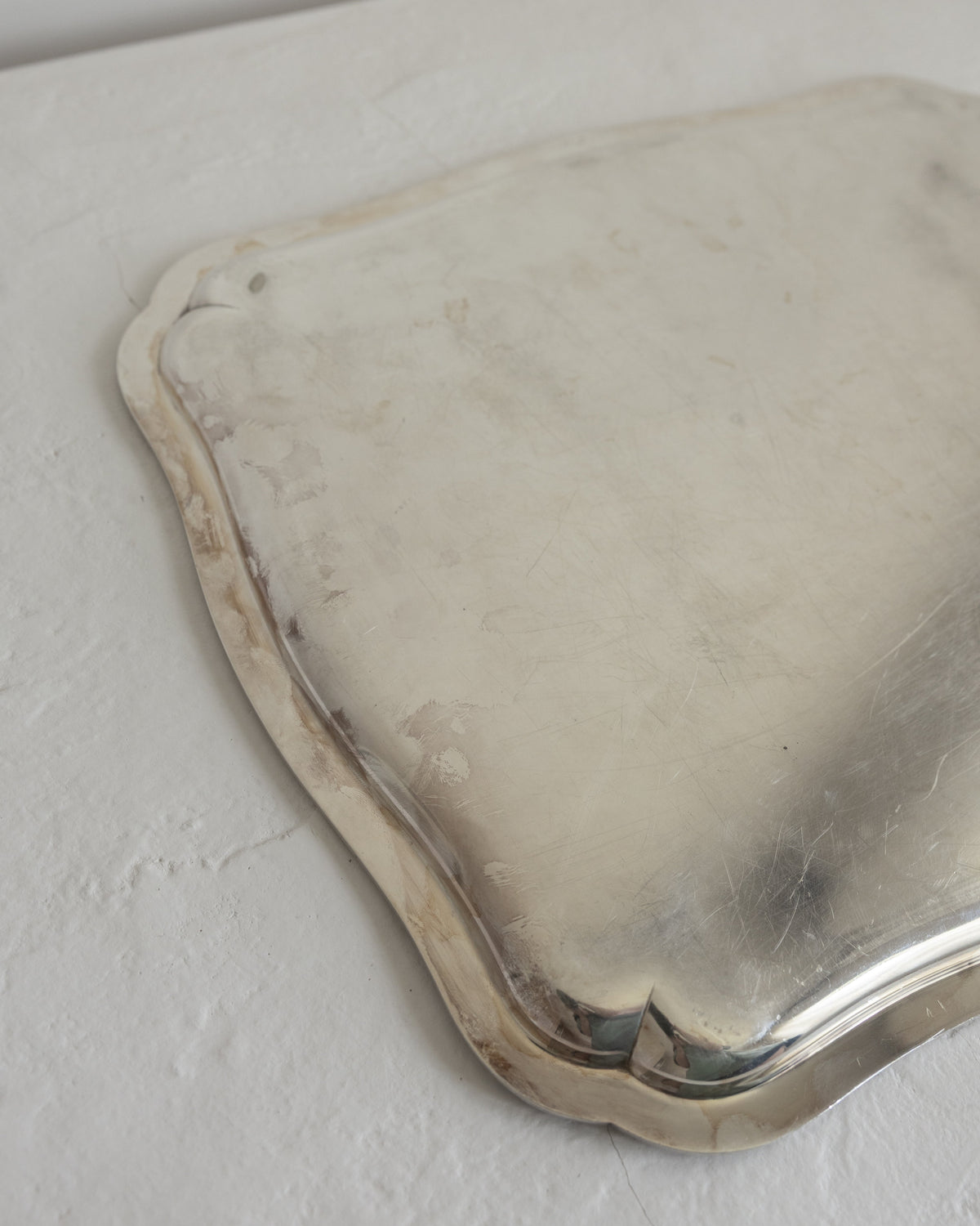 A vintage silver serving tray with scalloped edges, shown from an overhead angle on a textured off-white surface.