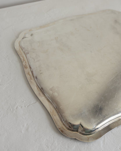 A vintage silver serving tray with scalloped edges, shown from an overhead angle on a textured off-white surface.